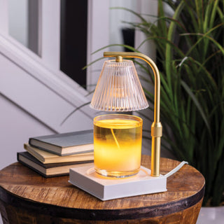 Luna Candle Warmer Lamp in gold with glass ribbed shade warming a yellow candle on a wooden table.