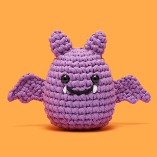 Luna the Bat crochet amigurumi in purple yarn with black eyes and white fangs on orange background
