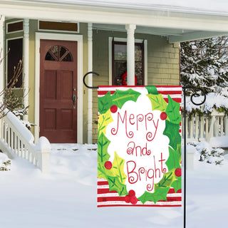 Studio M Merry and Bright garden flag with holly wreath displayed outside snowy home