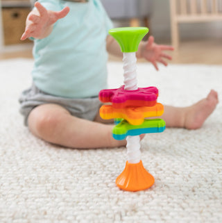 Baby reaching for colorful MiniSpinny stacking toy on white carpet by Fat Brain Toys