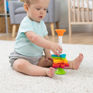 Baby playing with Fat Brain Toys MiniSpinny colorful stacking spinning toy on white carpet