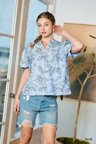 Woman wearing a blue floral blouse and denim shorts indoors.