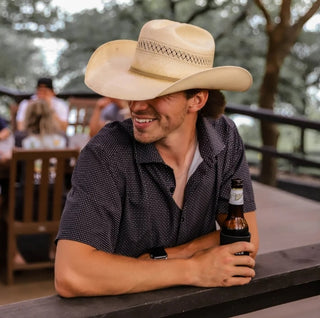 Man wearing a cowboy hat and holding a beer at an outdoor setting