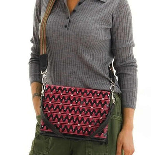 Person wearing a gray sweater and green pants with a red and black patterned bag.