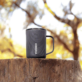 Corkcicle 16oz Burnt Wood insulated mug with handle sitting on a tree stump outdoors