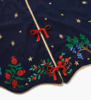 Rifle Paper Co. navy velvet Christmas tree skirt with embroidered pomegranates, botanicals, gold stars, and red ribbon ties.