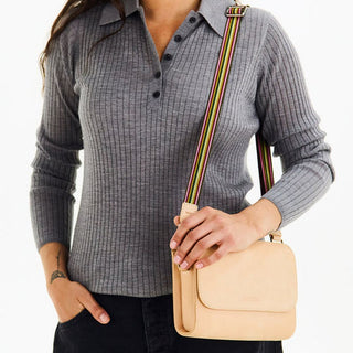 Woman wearing tan crossbody bag with colorful striped webbing strap over grey ribbed shirt