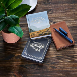 Two editions of One-Minute Devotions for Men displayed on rustic wooden surface with journal and pen.