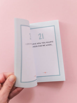 Hand holding open a prompted journal with page reading 'I Love How You Always Cheer For Me When...'