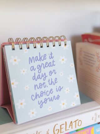 Desk flip calendar displaying motivational quote surrounded by daisy flowers on light blue background