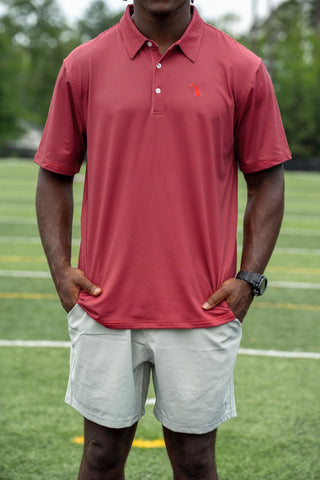 Man wearing red and black striped Local Boy Outfitters polo shirt on athletic field