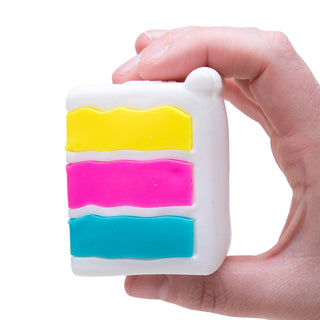 Hand holding a white layered cake-shaped Needoh stress toy with yellow, pink, and teal filling.
