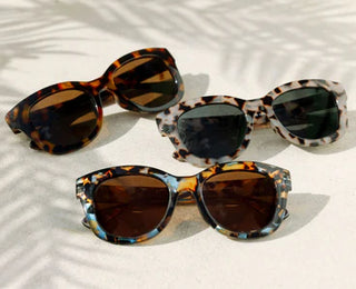 Three Peepers reading glasses in amber, gray, and blue tortoise patterns on palm leaf shadow