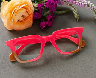 Pink and tan two-tone reading glasses styled with flowers on gray surface