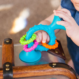 Baby hand playing with Fat Brain Toys PipSquigz Loops in teal with colorful rings attached.
