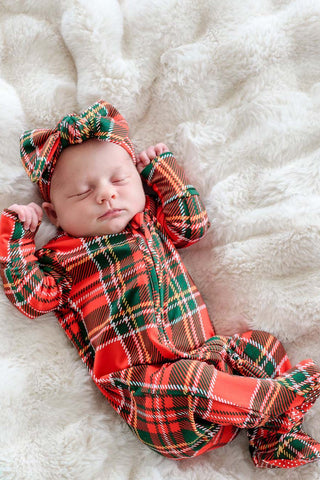 Sleeping newborn wearing Caden Lane red and green plaid Christmas zipper footie with matching bow headband