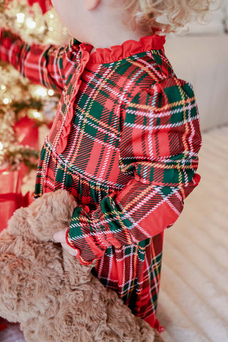 Toddler girl wearing red and green plaid Christmas nightgown with ruffle trim, holding teddy bear