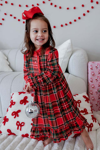 Young girl wearing red tartan plaid Christmas nightgown with ruffle hem and red bow hair clip