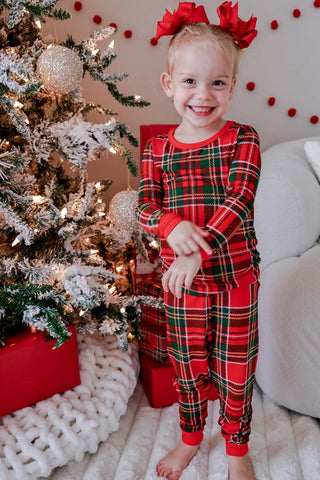 Toddler wearing red and green plaid bamboo two-piece Christmas pajama set near decorated tree