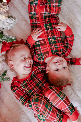 Two children laughing in matching red and green plaid Christmas bamboo pajamas by Caden Lane