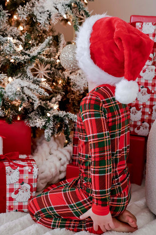 Child wearing red and green plaid bamboo pajama set with Santa hat near Christmas tree