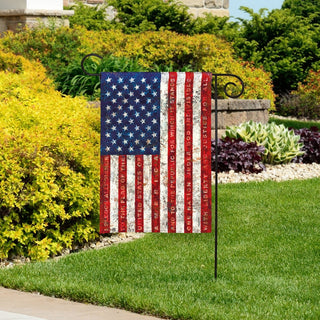 Distressed American flag garden decor hanging beside colorful garden foliage and stone wall
