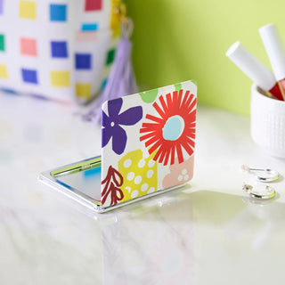 Colorful floral patterned compact pocket mirror open on marble surface with accessories