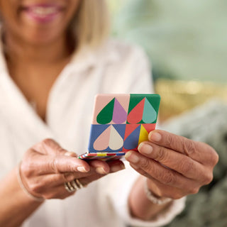 Woman holding a colorful geometric patterned square pocket mirror with teardrop shapes