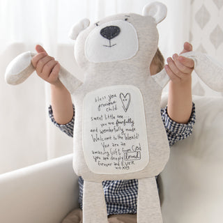 Child holding light gray bear plush toy with inspirational message on belly