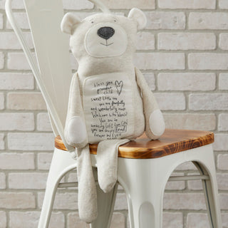 Light gray stuffed bear with inspirational message printed on belly, seated on white chair