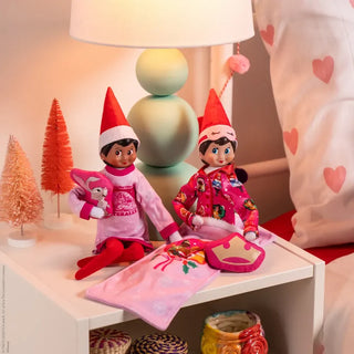 Two Elf on the Shelf dolls in pink Disney princess pajamas with sleep masks and blanket