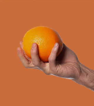 Hand holding a fresh orange against an orange background, representing Poo-Pourri Trap-A-Crap citrus scent