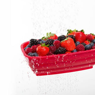 Red collapsible berry colander filled with mixed berries being rinsed under running water