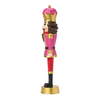 Pink and gold nutcracker figurine with crown, brown hair, red pants, and black boots on gold base