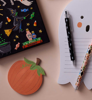 Pumpkin-shaped orange sticky note pad displayed alongside Halloween-themed stationery accessories