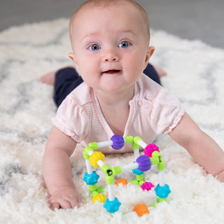 Baby doing tummy time on white rug playing with colorful Quubi sensory toy by Fat Brain Toys