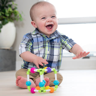 Happy baby playing with colorful Fat Brain Toys Quubi sensory cube toy on floor
