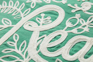 Close-up detail of white embroidered script and floral motifs on green pillow fabric.