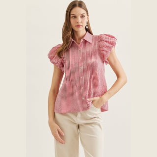 Woman wearing a red and white checkered blouse with ruffled sleeves on a plain background