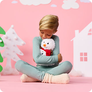 Child hugging a white plush snowman with red scarf Warmies stuffed animal toy