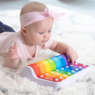Baby girl playing with Fat Brain Toys Rock N Roller Piano rainbow xylophone on white carpet