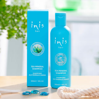 Inis Sea Mineral Shampoo bottle and packaging on a wooden surface with blurred greenery in the background