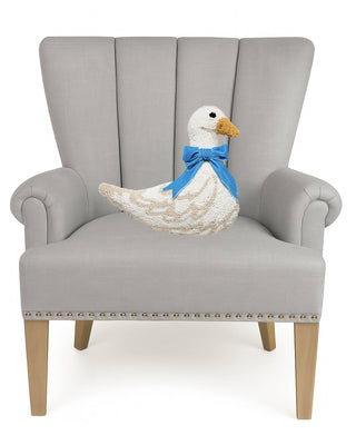 White hooked wool goose pillow with blue velvet bow, displayed on gray armchair