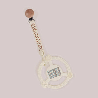 Off-white silicone teether ring with raised dots spiral and ribbed textures, embossed Howdy text, cream polka dot strap, and wood clip