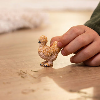 Child's hand holding a Schleich Silkie Chicken miniature figurine on a wooden surface
