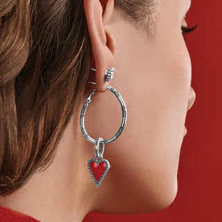 Silver hoop earring with red enamel heart charm worn on ear against red background