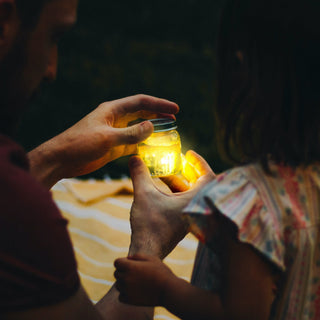 Adult and child sharing a glowing mason jar filled with light-up Glo Pals at dusk