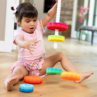 Toddler girl playing with Fat Brain Toys SpinAgain stacking spin toy on hardwood floor.