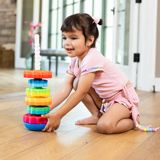 Young toddler girl playing with Fat Brain Toys SpinAgain rainbow stacking spinner toy on floor.