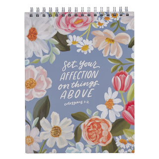 Spiral-bound notepad with floral design and Colossians 3:2 Bible verse on blue background